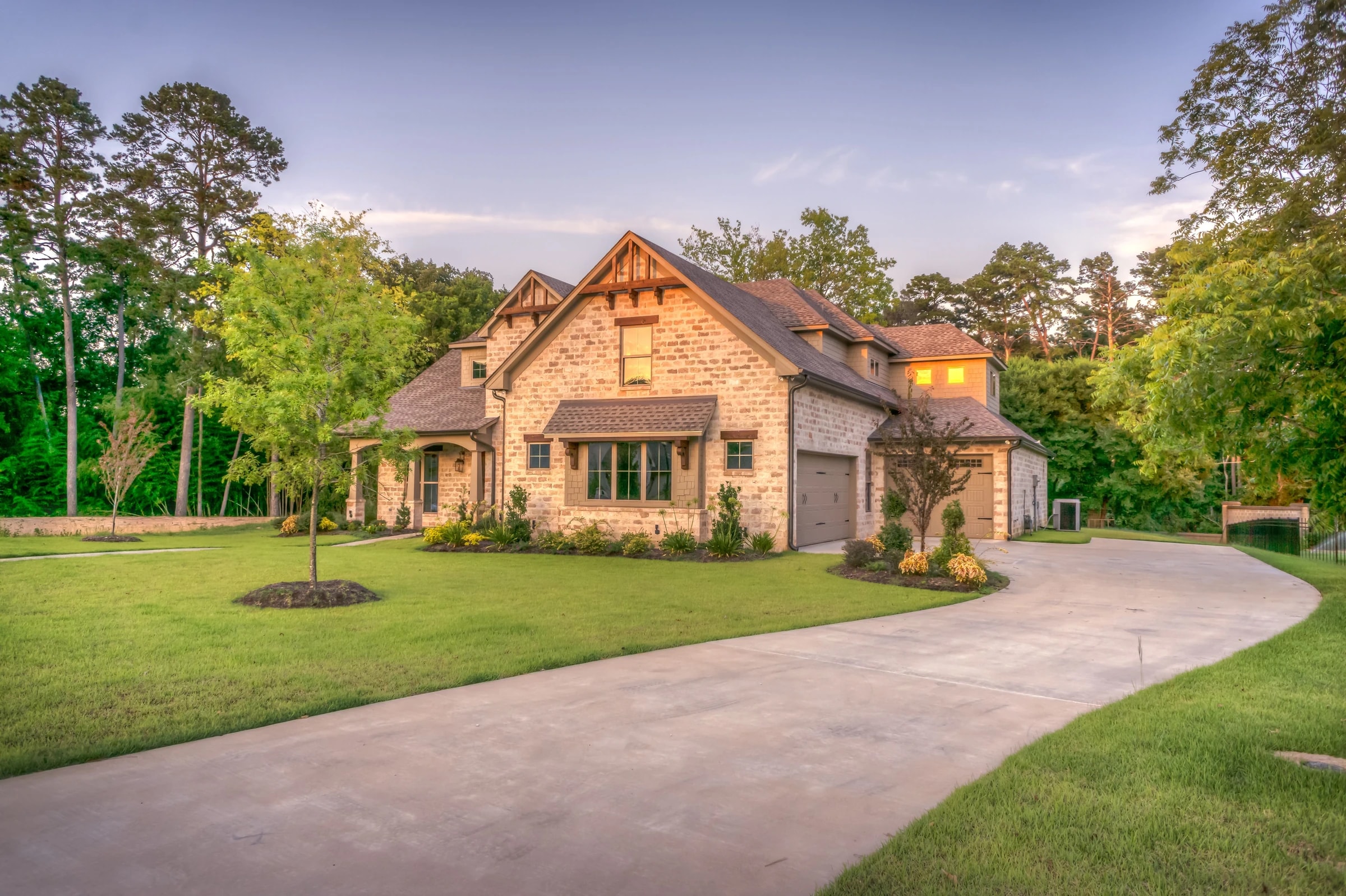Stone suburban home with driveway and mature trees at golden hour
